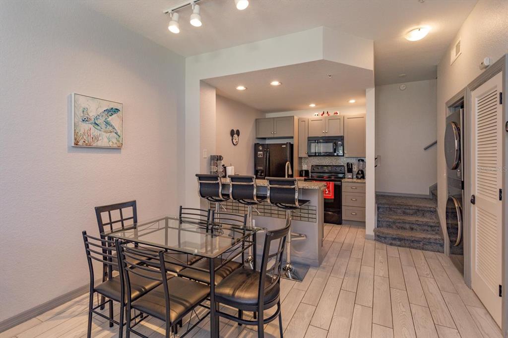 A dining area with a glass table and breakfast bar opens into a modern kitchen — 2211 SAN VITTORINO CIRCLE UNIT 103, KISSIMMEE, FL