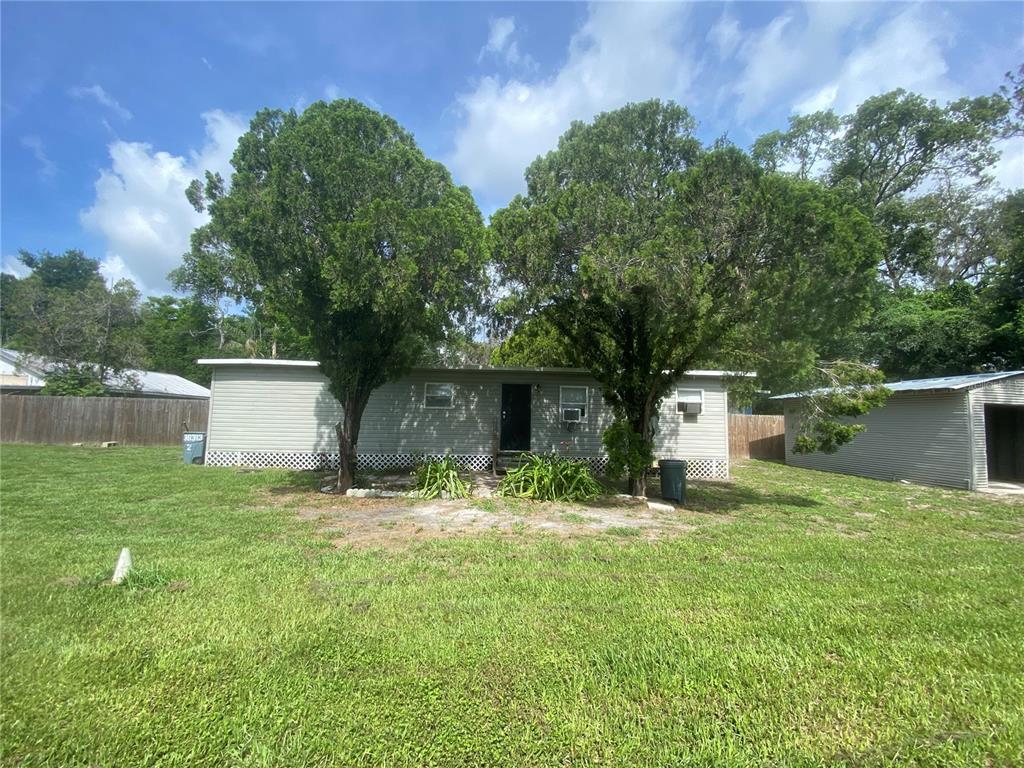 A single-story house with light gray siding sits behind two large trees on a lawn — 38313 TUCKER ROAD UNIT 3, ZEPHYRHILLS, FL