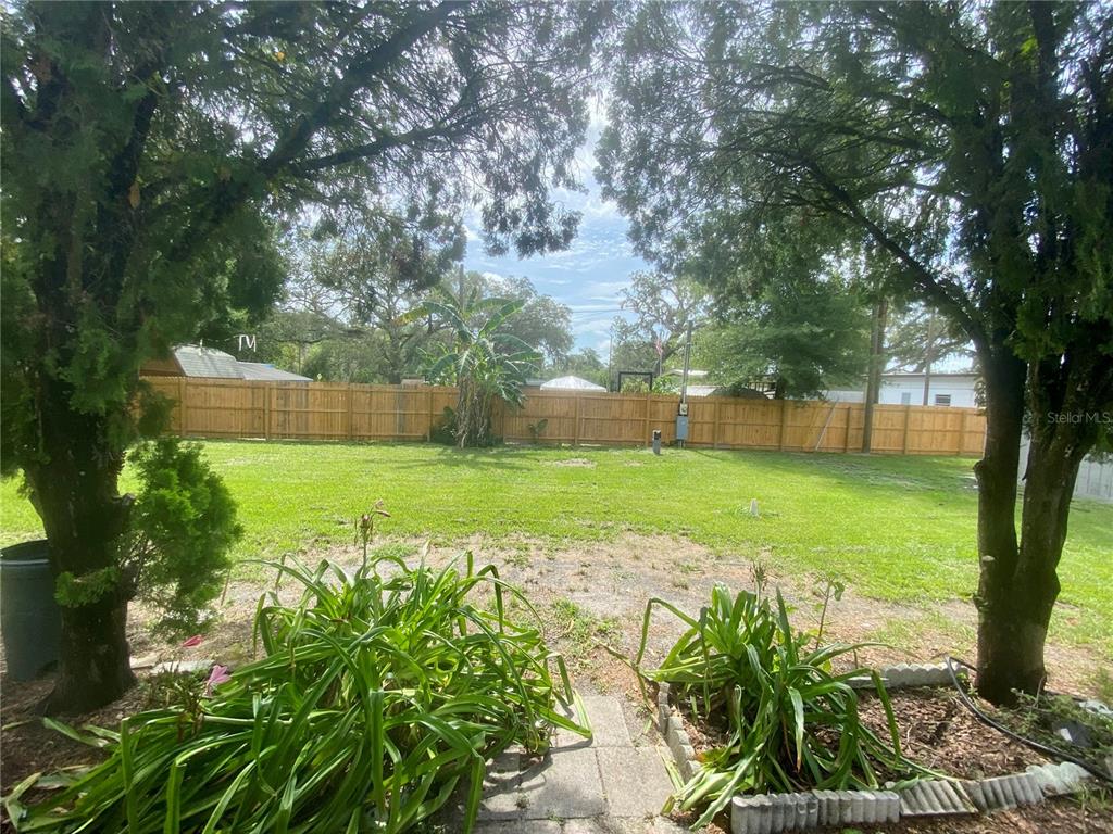 A grassy backyard features a wooden fence, mature trees, and two small garden beds — 38313 TUCKER ROAD UNIT 3, ZEPHYRHILLS, FL