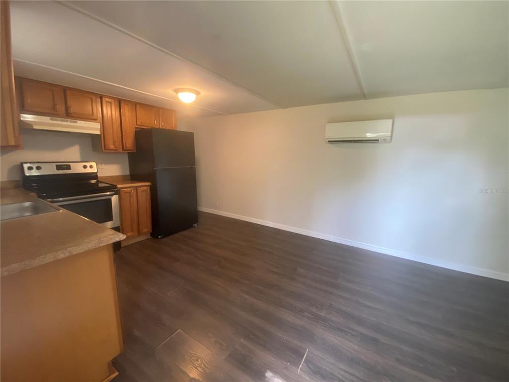 A kitchen with wood cabinets, black appliances, and dark wood-look flooring opens to a living area — 38313 TUCKER ROAD UNIT 3, ZEPHYRHILLS, FL