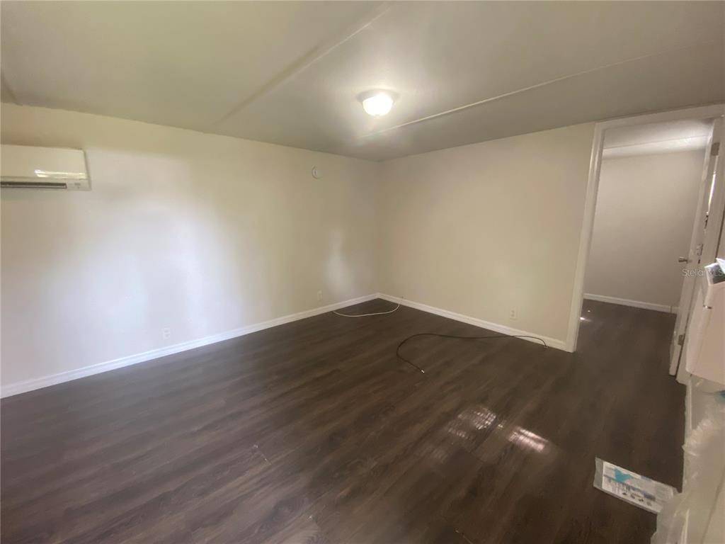 An empty room features light-colored walls, dark wood-look flooring, and a wall-mounted air conditioner — 38313 TUCKER ROAD UNIT 3, ZEPHYRHILLS, FL