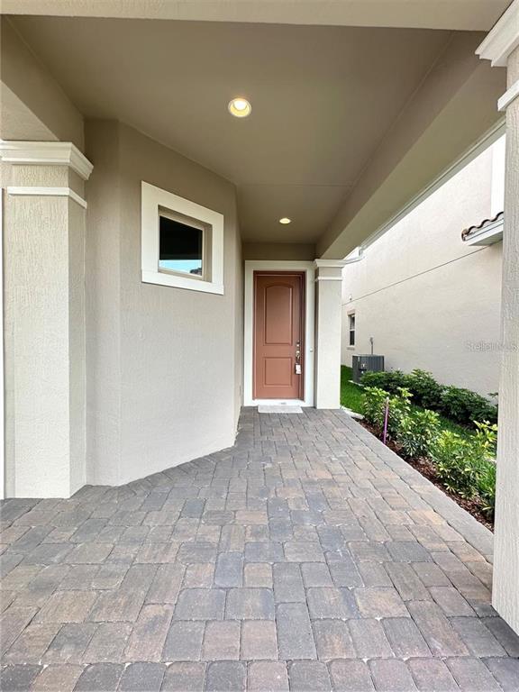A covered entryway features a brown front door, a small window, and paved flooring — 13112 WEAVER AVENUE, ORLANDO, FL