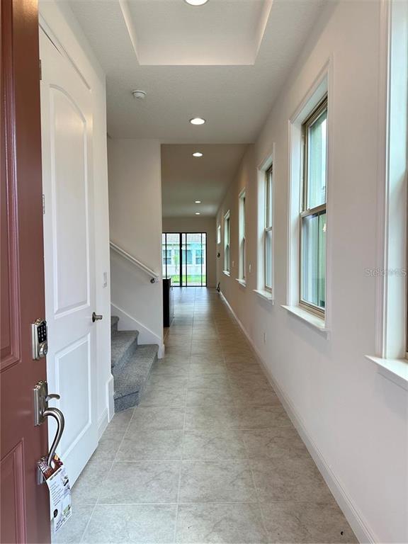 A long, tiled entryway leads past a staircase toward a bright, open living area — 13112 WEAVER AVENUE, ORLANDO, FL