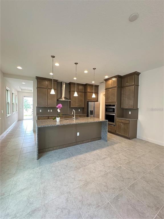 A kitchen features dark wood cabinets, a granite-topped island, and light-colored tile flooring — 13112 WEAVER AVENUE, ORLANDO, FL