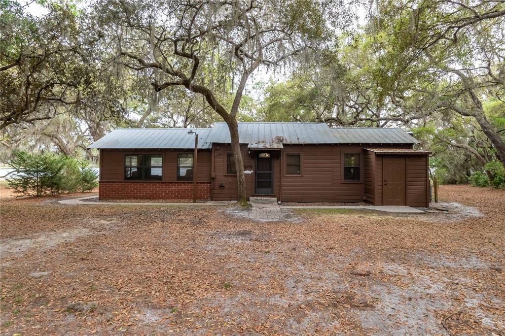 A brown, single-story cabin with a metal roof sits among trees on a leaf-covered lot — 22649, 22645 and TBD NE 105TH AVENUE ROAD, FORT MC COY, FL
