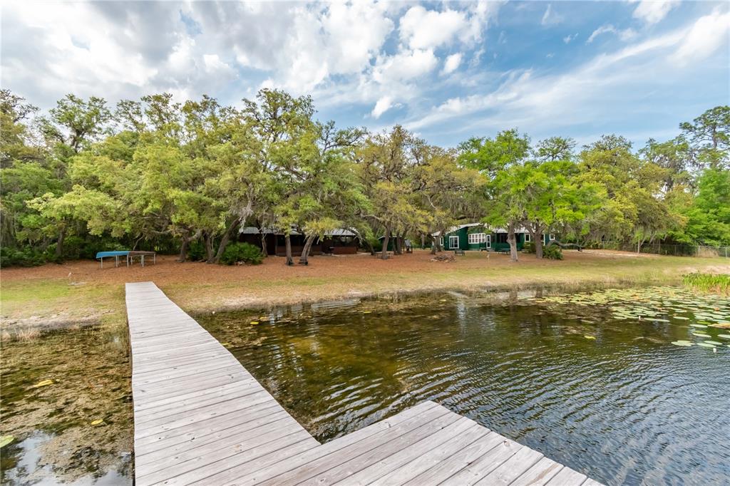 A wooden dock extends into a pond in front of a house nestled among trees — 22649, 22645 and TBD NE 105TH AVENUE ROAD, FORT MC COY, FL