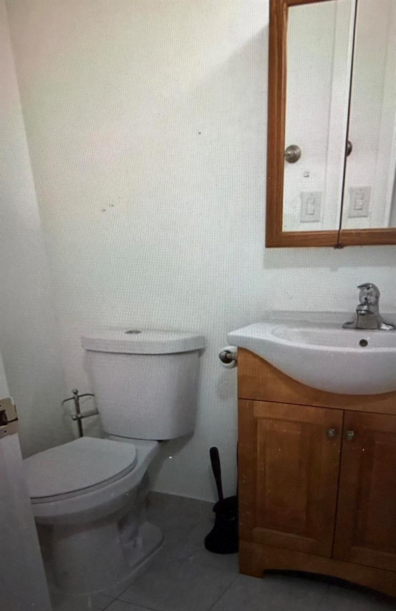 A small bathroom featuring a white toilet, a wooden vanity with a sink, and a mirror — 2038 Exeter C, Boca Raton FL 33434, BOCA RATON, FL