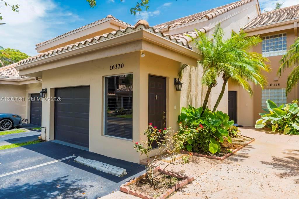 The exterior of a tan townhouse features a garage, a front door, and a palm tree — 16320 Malibu Dr # 10, Weston FL 33326, WESTON, FL