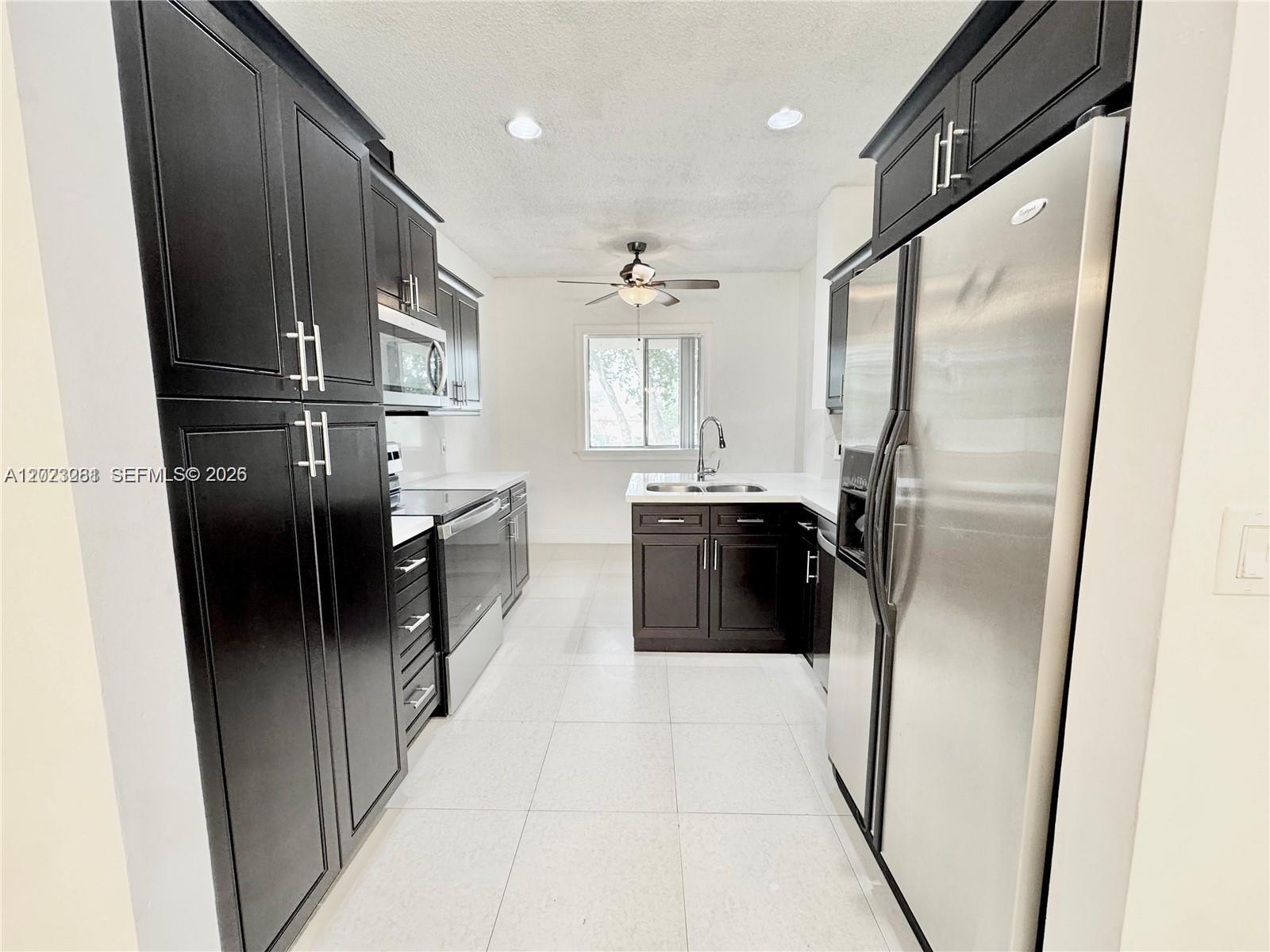 A galley kitchen features dark wood cabinets, stainless steel appliances, and white tile flooring — 16320 Malibu Dr # 10, Weston FL 33326, WESTON, FL