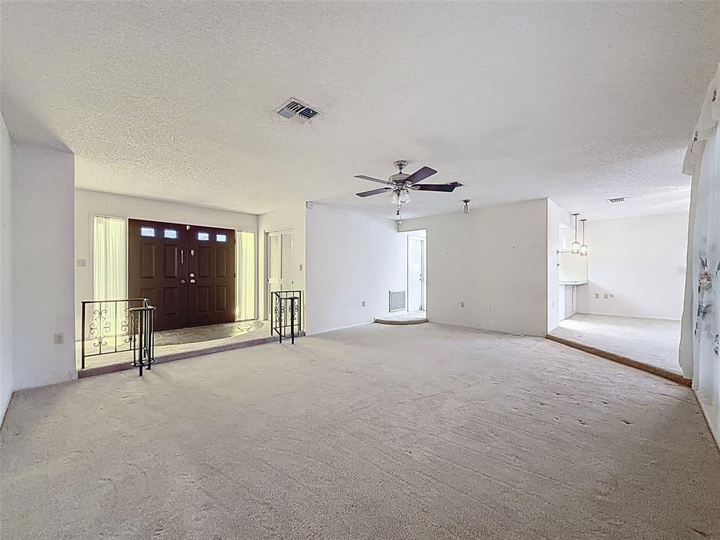 A spacious living room features beige carpeting, a ceiling fan, and a sunken entryway — 9811 WOODSTOCK LANE, PORT RICHEY, FL