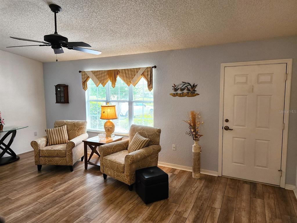 A living room features two patterned armchairs, a side table, a ceiling fan, and wood-look flooring — 11660 SW 89TH TERRACE, OCALA, FL