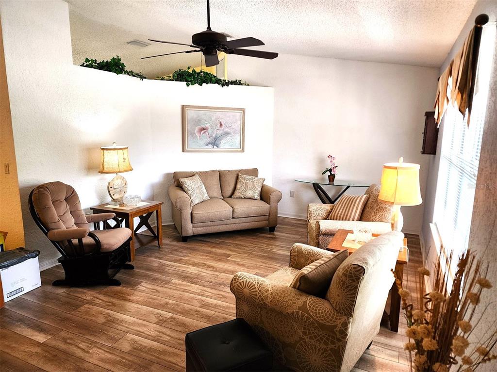 A living room features wood-look flooring, a ceiling fan, and a mix of neutral-toned furniture — 11660 SW 89TH TERRACE, OCALA, FL
