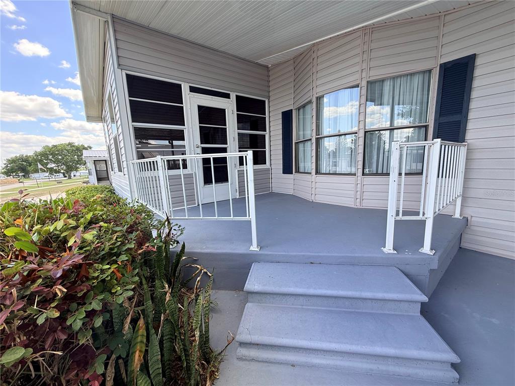 A gray painted porch with white railings and steps leads to a screened-in entryway — 116 S WINTER CIRCLE, AVON PARK, FL