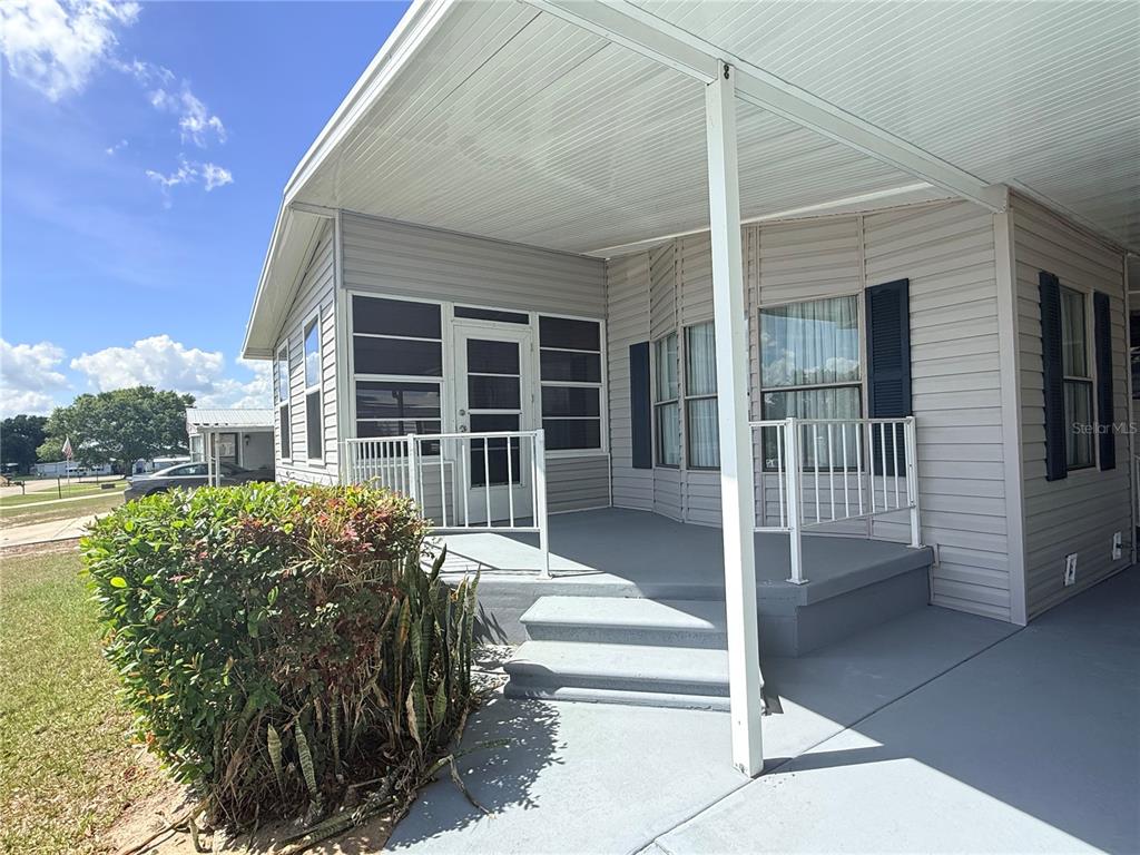 A covered porch with a screened-in entrance and white railings sits beside a light-colored home — 116 S WINTER CIRCLE, AVON PARK, FL