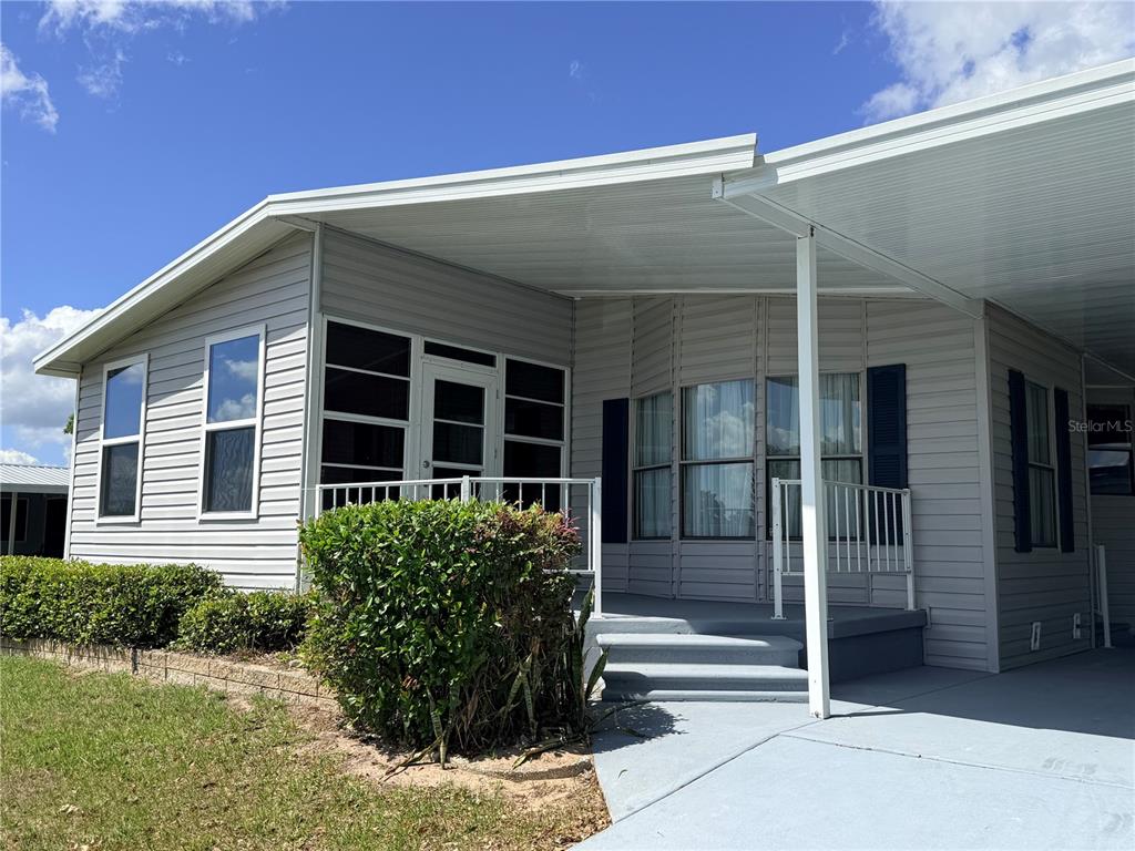 A light gray manufactured home features a screened-in porch, a carport, and a small front lawn — 116 S WINTER CIRCLE, AVON PARK, FL