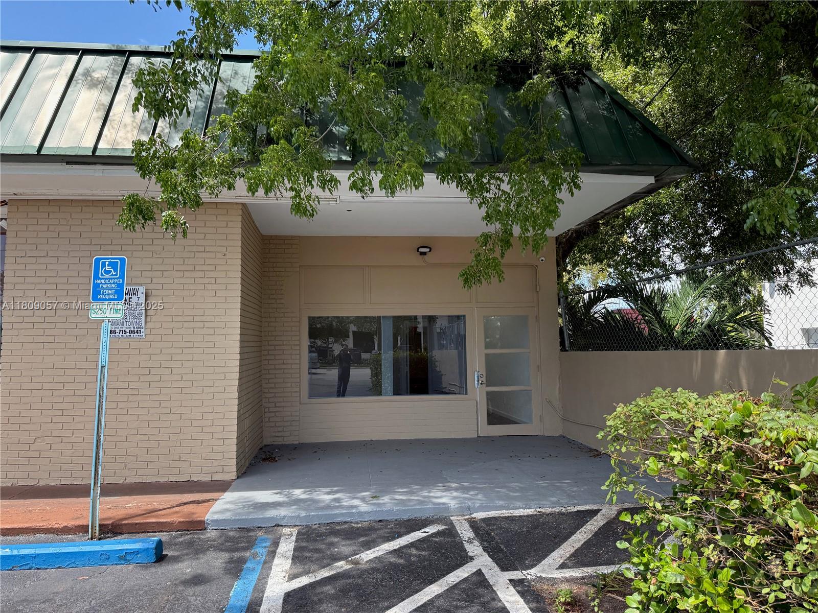 A tan brick building exterior features a green metal roof, a glass door, and parking — 8320 SW 124th St, Pinecrest FL 33156, PINECREST, FL