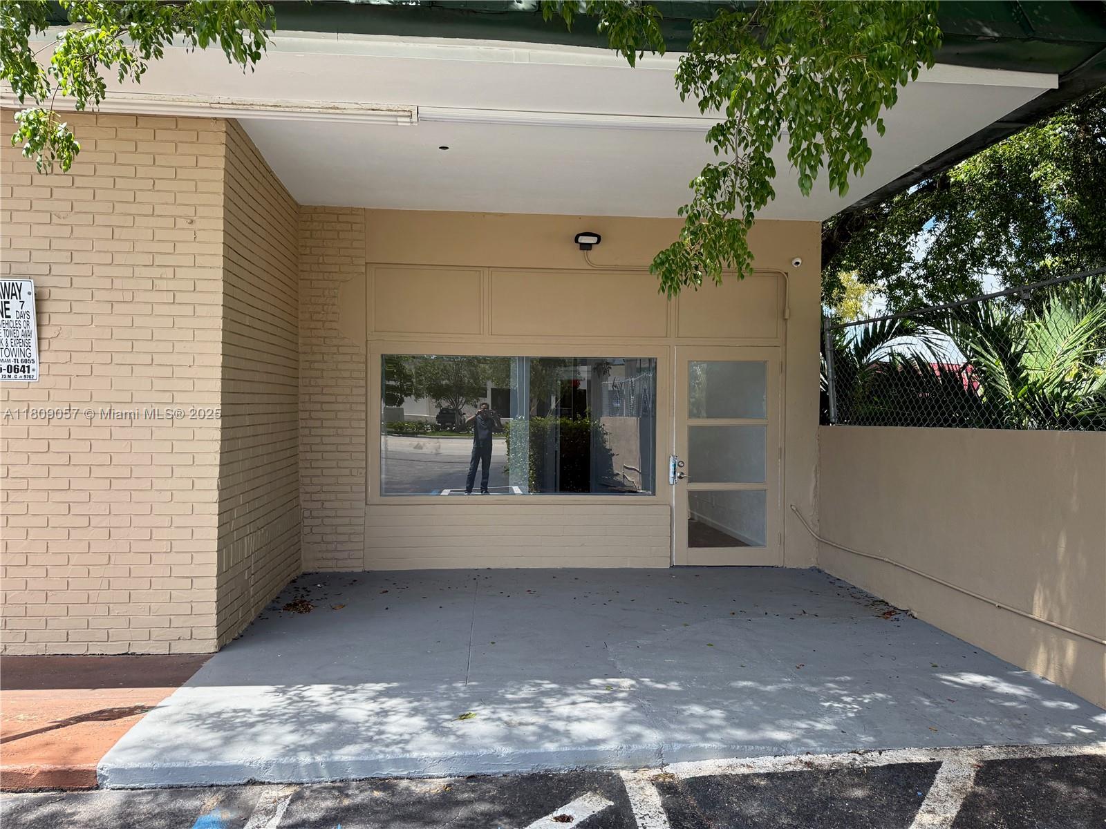 A beige brick building exterior features a glass storefront window and a glass-paneled door — 8320 SW 124th St, Pinecrest FL 33156, PINECREST, FL