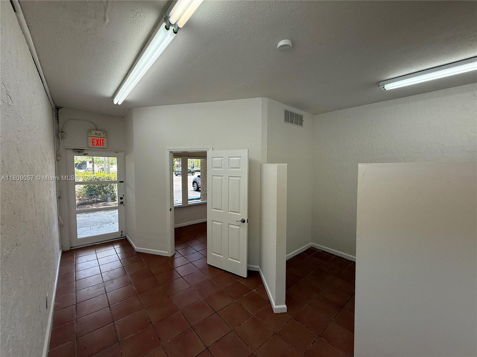An interior office space features white walls, tile flooring, fluorescent lighting, and an exit door — 8320 SW 124th St, Pinecrest FL 33156, PINECREST, FL