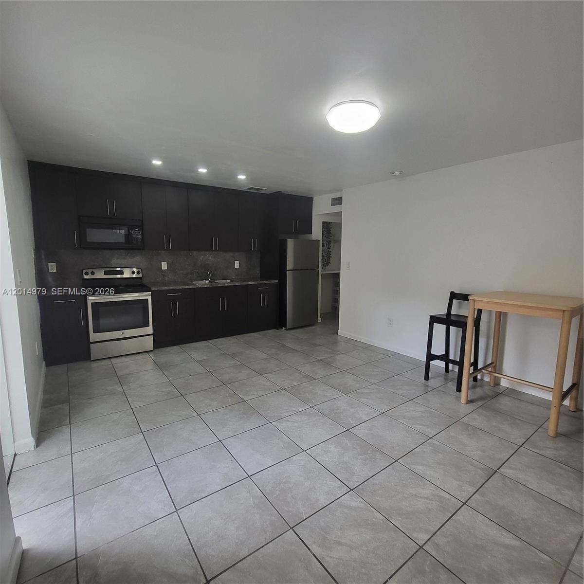 A kitchen features dark cabinetry, stainless steel appliances, and light gray tile flooring — 315 NW 59th St # 2, Miami FL 33127, MIAMI, FL