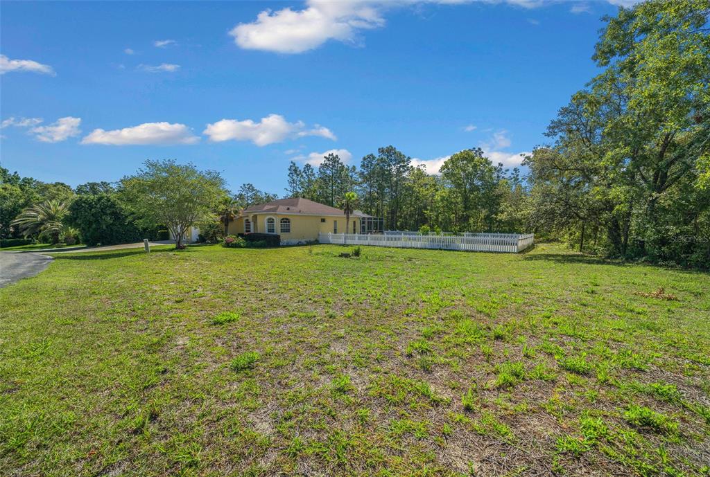 A yellow house with a white picket fence sits on a large, grassy lot — 9 GREVILLEA COURT, HOMOSASSA, FL