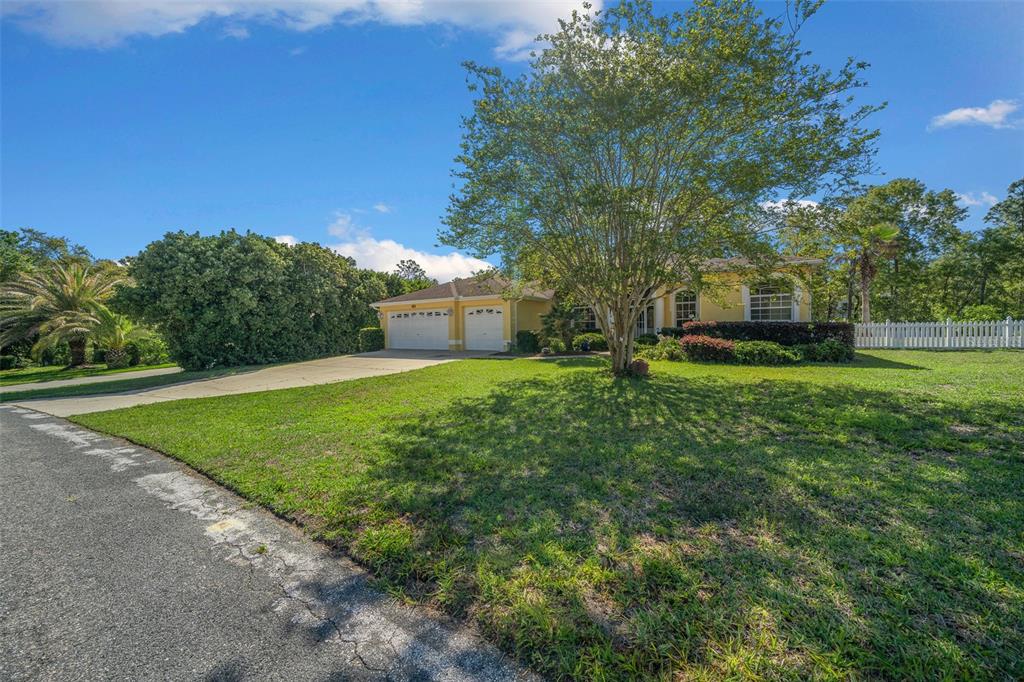 A yellow single-story house with a two-car garage and a large tree in the yard — 9 GREVILLEA COURT, HOMOSASSA, FL
