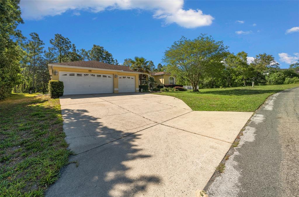 A yellow house with a three-car garage and a large concrete driveway under a blue sky — 9 GREVILLEA COURT, HOMOSASSA, FL