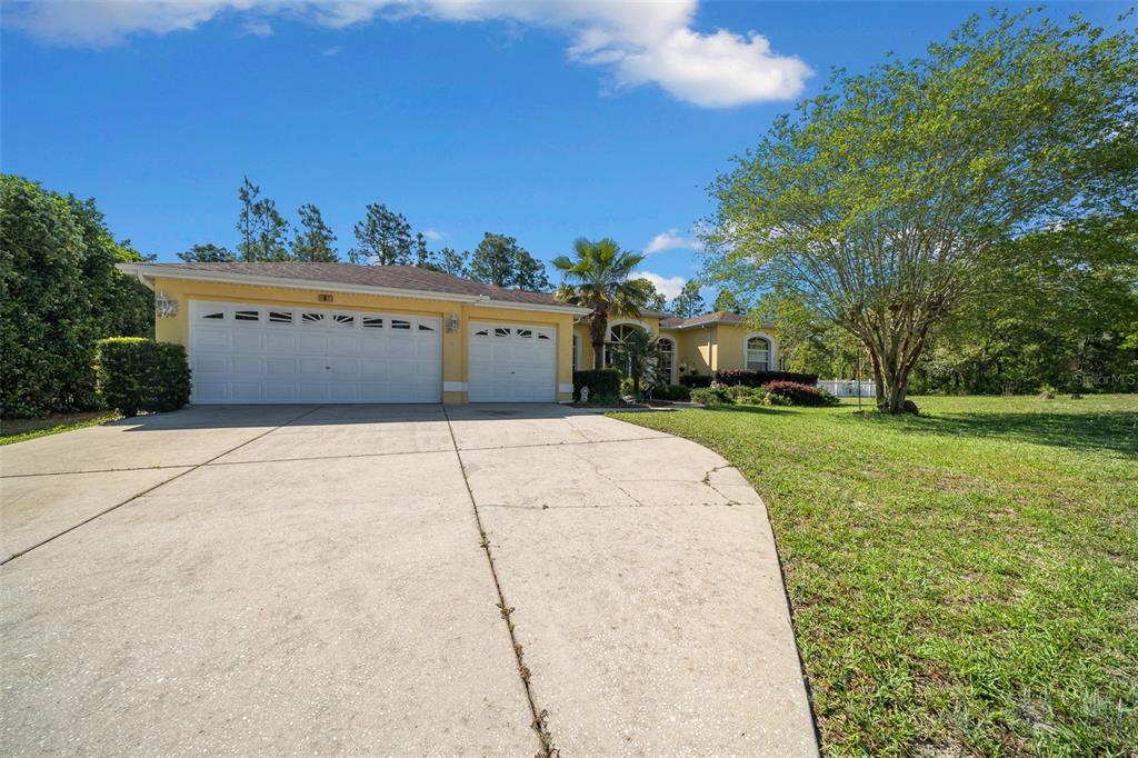 A yellow single-story house with a three-car garage and a large concrete driveway — 9 GREVILLEA COURT, HOMOSASSA, FL