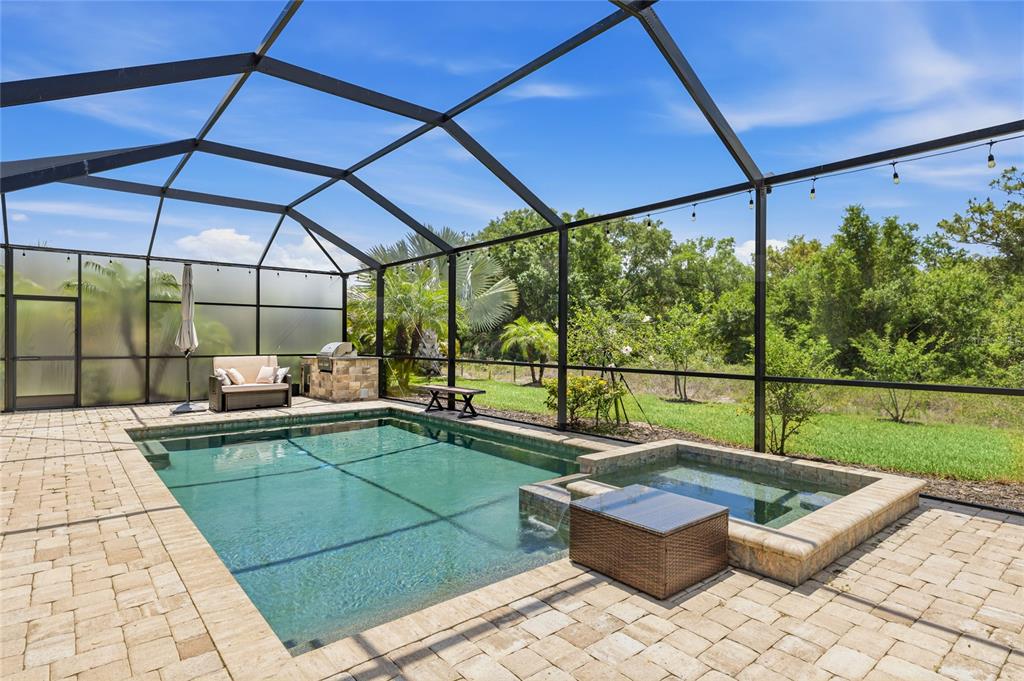 A screened-in patio features a rectangular swimming pool, a raised spa, and stone pavers — 17821 POLO TRAIL, BRADENTON, FL