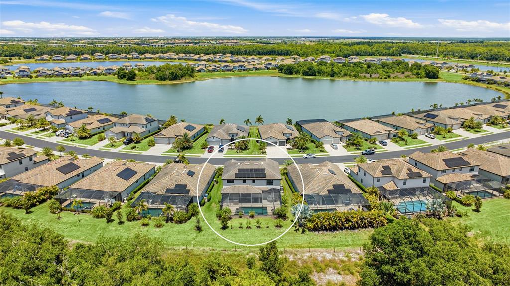An aerial view shows a two-story house with a pool and solar panels near a lake — 17821 POLO TRAIL, BRADENTON, FL