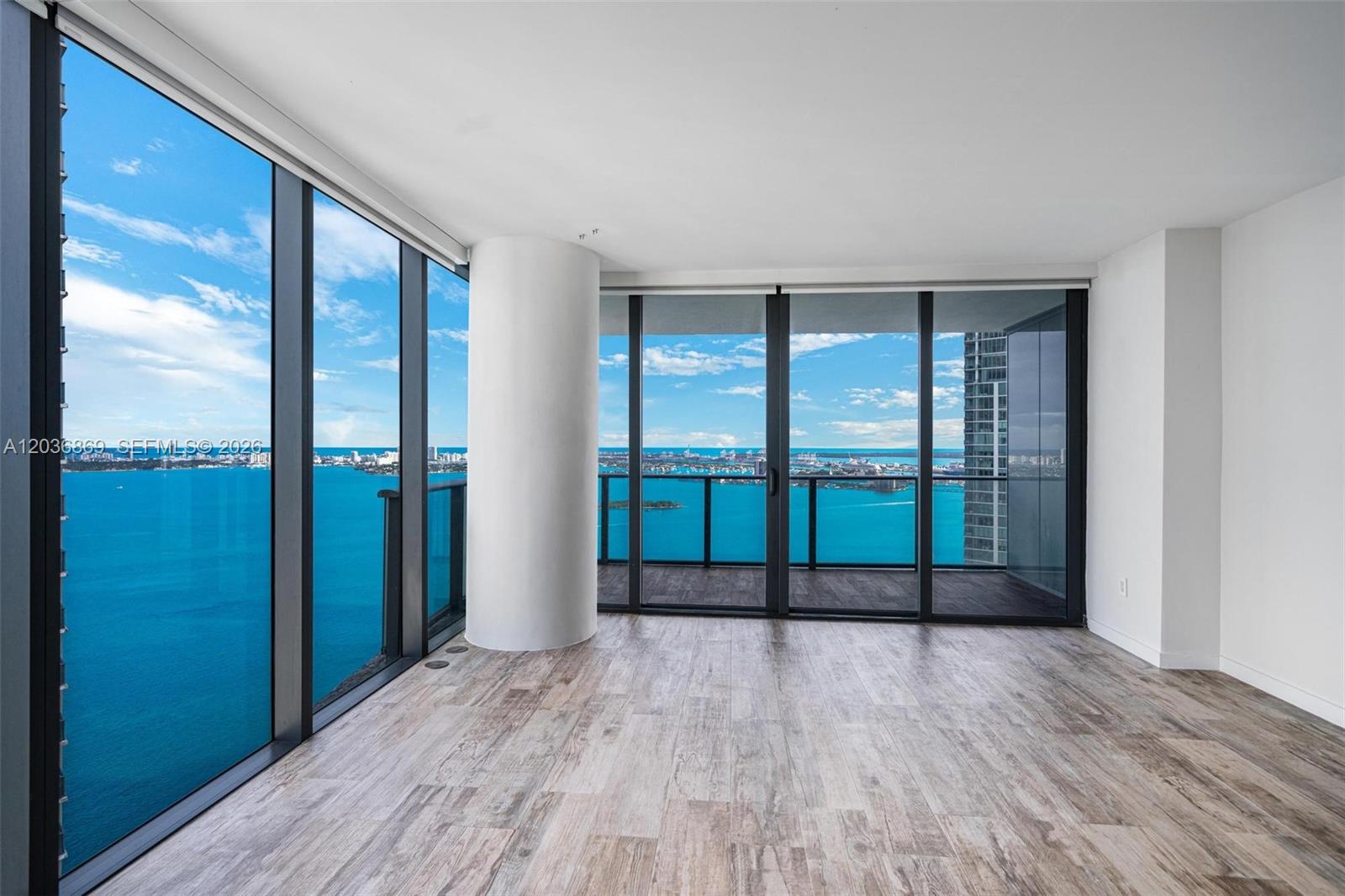 An empty room features wood-look flooring, a structural column, and floor-to-ceiling windows overlooking the ocean — 650 NE 32nd St # 4407, Miami FL 33137, MIAMI, FL