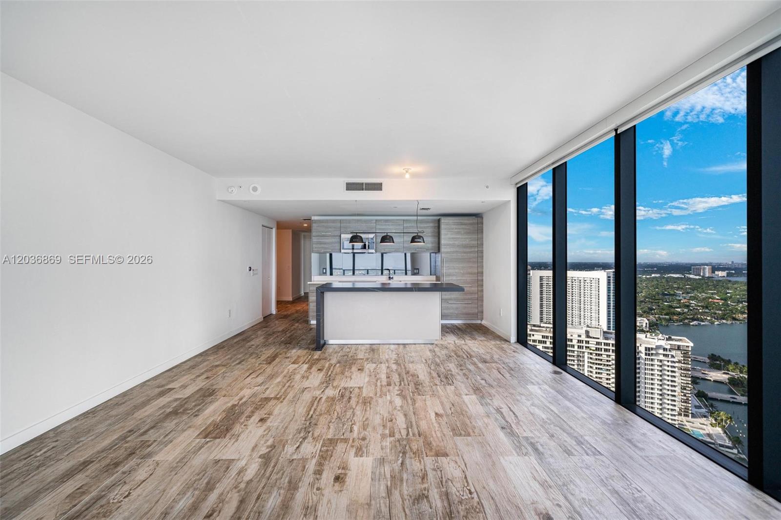 A modern kitchen with a breakfast bar overlooks a living area with floor-to-ceiling windows — 650 NE 32nd St # 4407, Miami FL 33137, MIAMI, FL