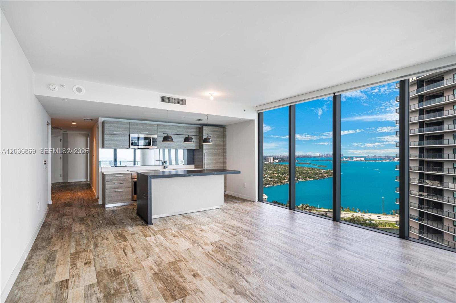 A modern kitchen with an island overlooks a bay through floor-to-ceiling windows — 650 NE 32nd St # 4407, Miami FL 33137, MIAMI, FL