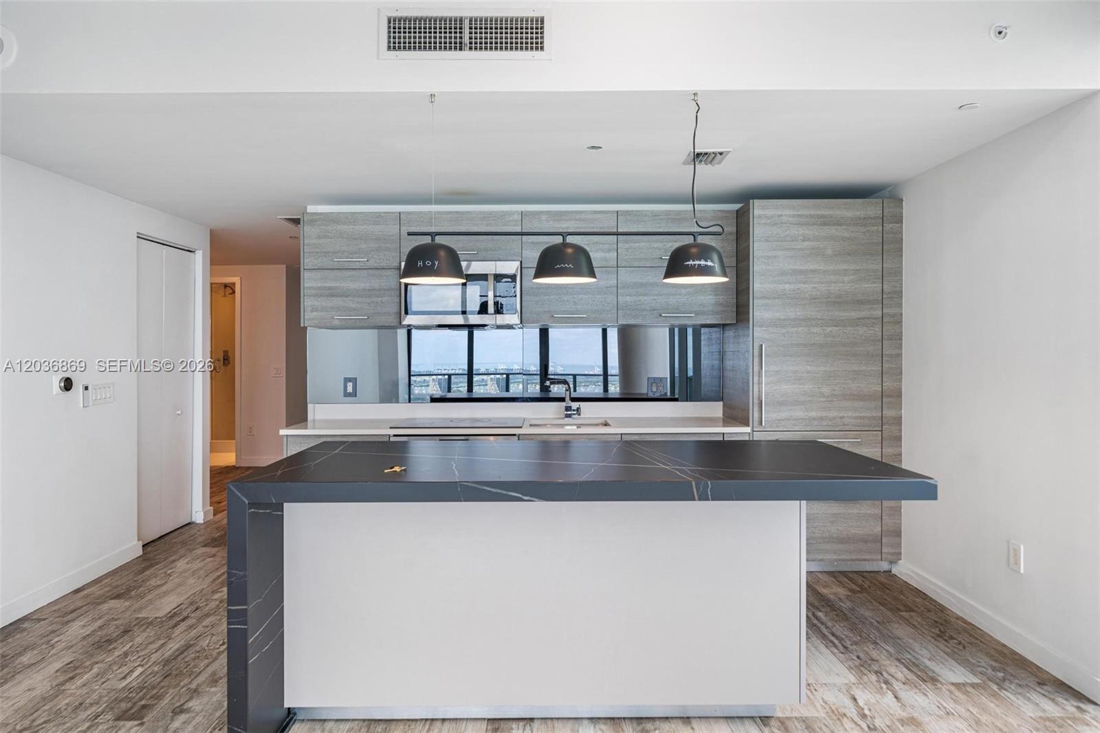 A modern kitchen features a waterfall island, gray wood-grain cabinetry, and a mirrored backsplash — 650 NE 32nd St # 4407, Miami FL 33137, MIAMI, FL