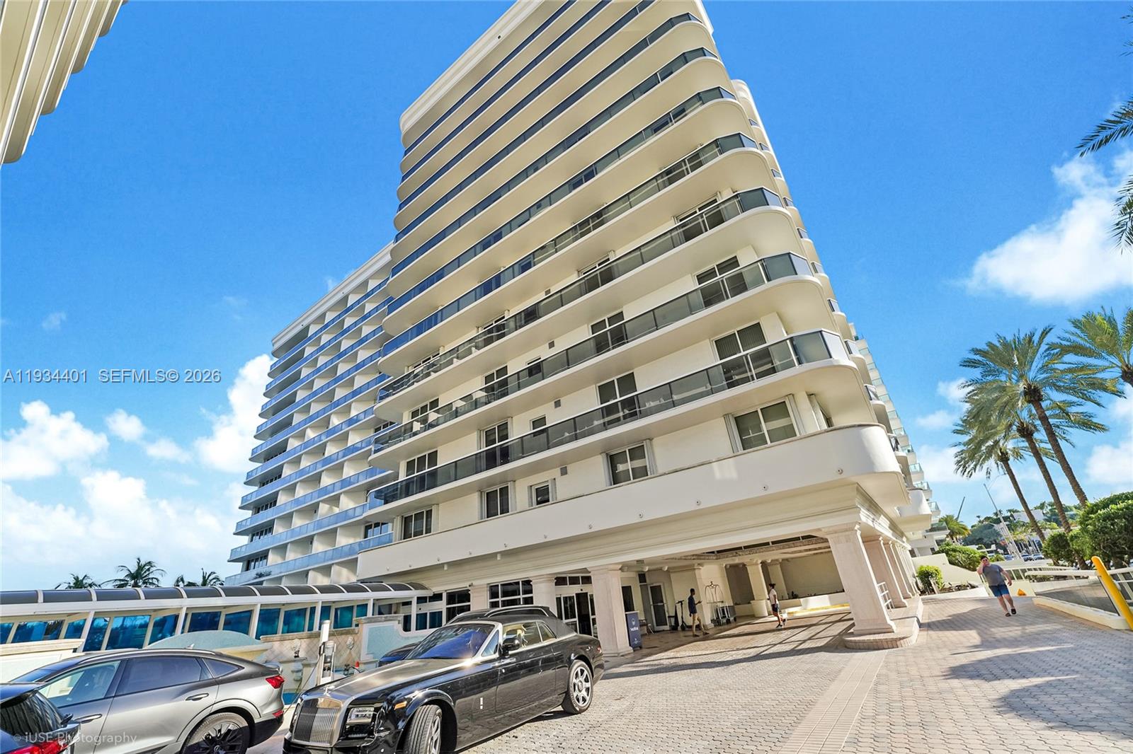 A low-angle exterior view shows a multi-story white apartment building with balconies and a driveway — 9559 Collins Ave # F, Surfside FL 33154, SURFSIDE, FL