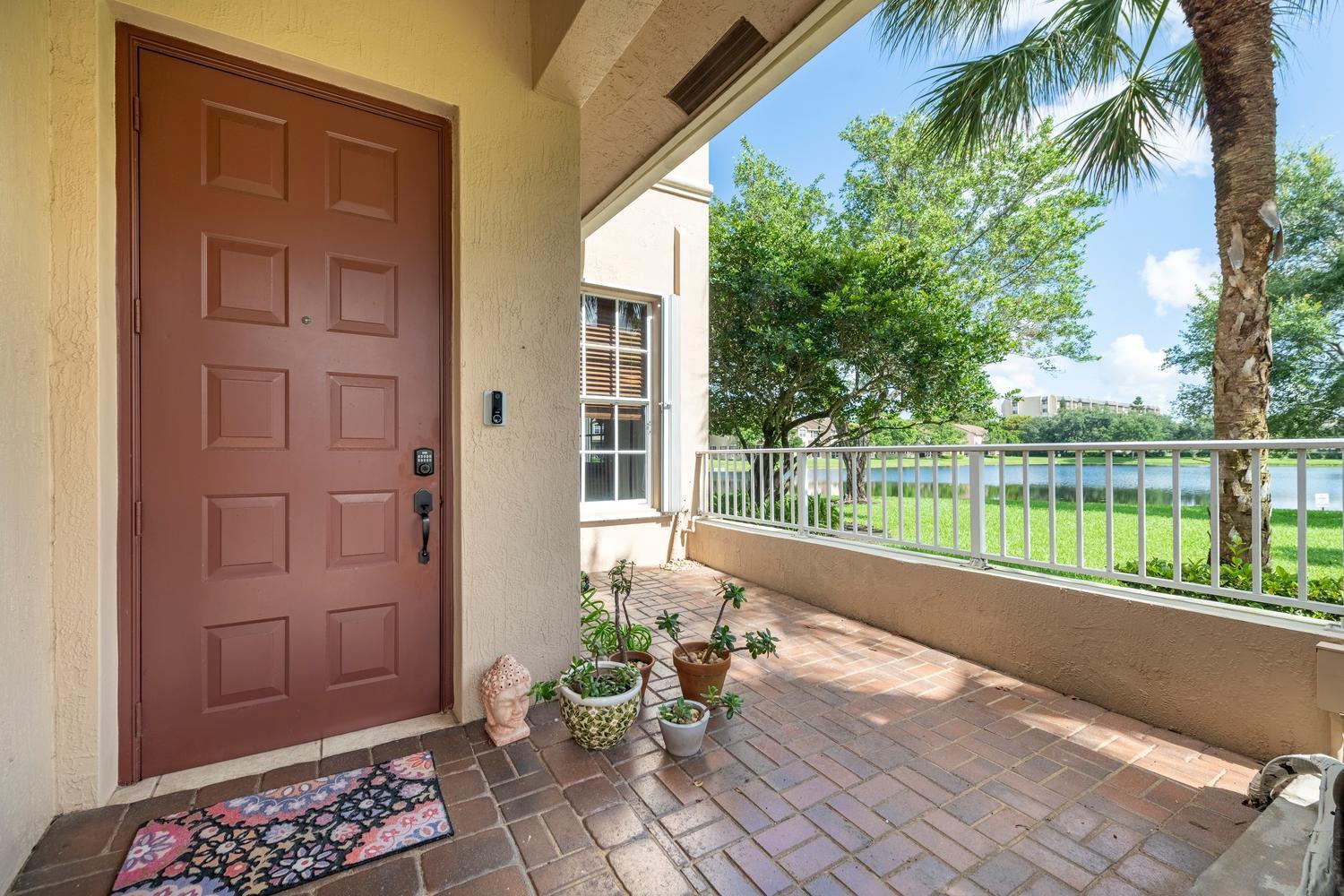 A brick-paved entryway features a brown door, potted plants, and a view of a lake — 3501 Lakeside Drive, Davie FL 33328, DAVIE, FL