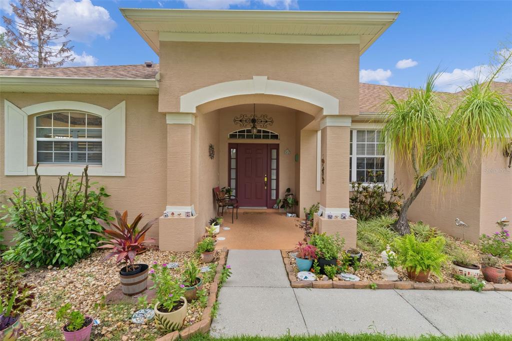 The exterior of a tan stucco house features a covered entryway with a red door — 2660 LEDGEMONT COURT, CLERMONT, FL