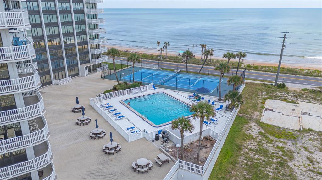 An aerial view shows a swimming pool, tennis courts, and a high-rise building by the ocean — 3580 S OCEAN SHORE BOULEVARD UNIT 404, FLAGLER BEACH, FL