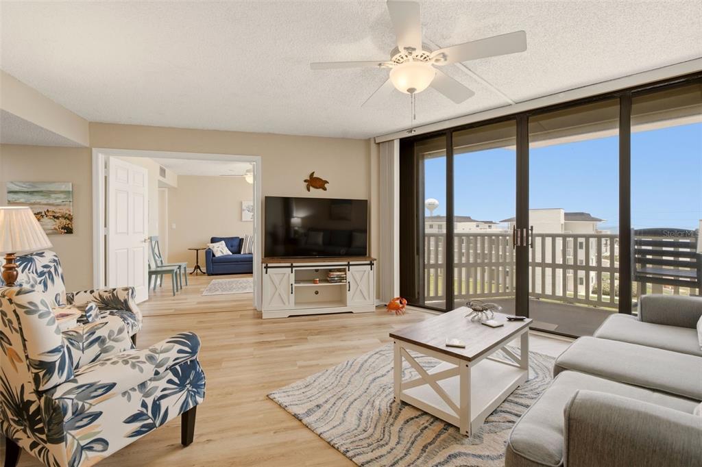 A living room features a floral armchair, a gray sofa, a television, and a balcony — 3580 S OCEAN SHORE BOULEVARD UNIT 404, FLAGLER BEACH, FL