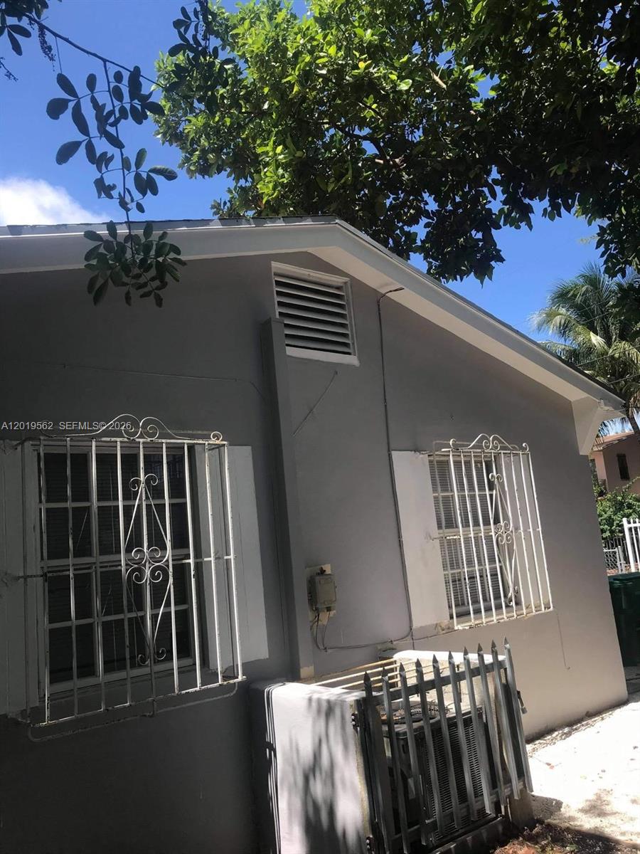 The exterior of a gray house features two windows with white security bars and a vent — MIAMI, FL