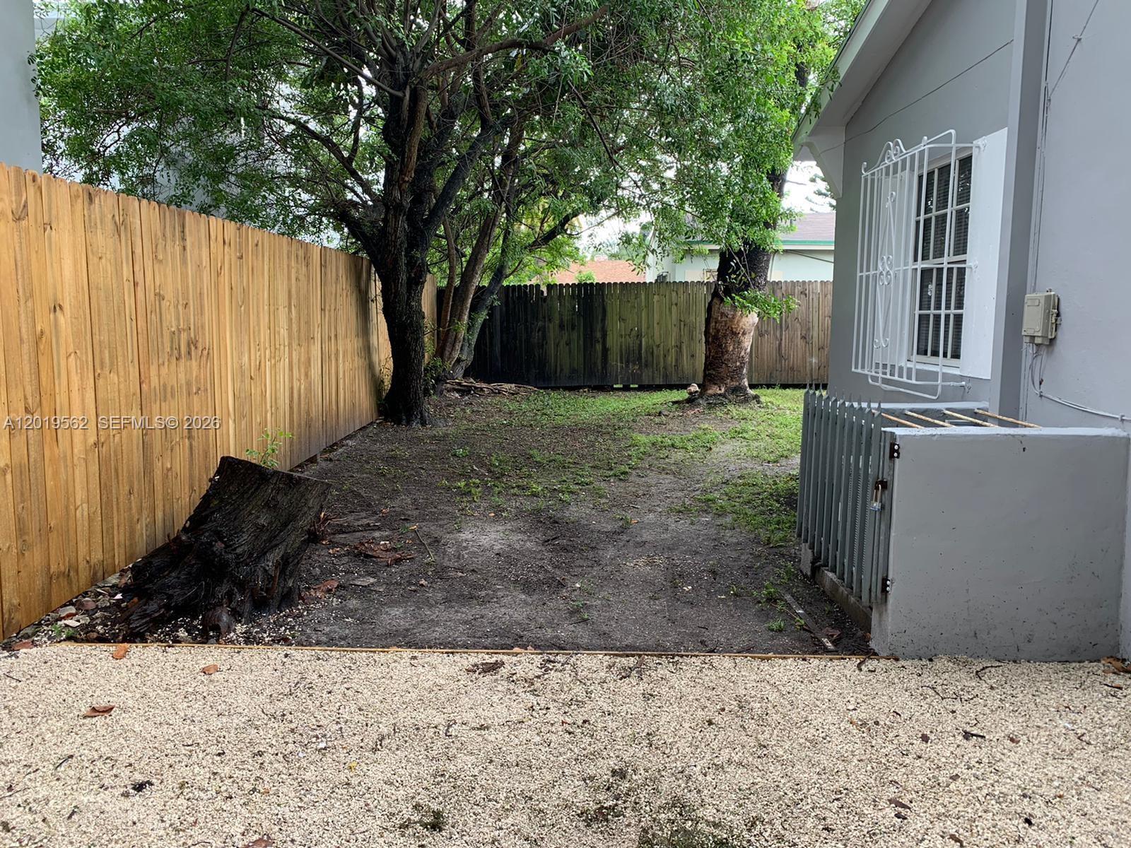 A backyard features a dirt lawn, a large tree stump, and a wooden fence — MIAMI, FL