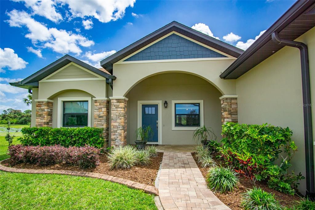 The exterior of a house features a stone-accented entryway, a blue front door, and landscaping — 8602 AMEN CORNER PLACE, PALMETTO, FL