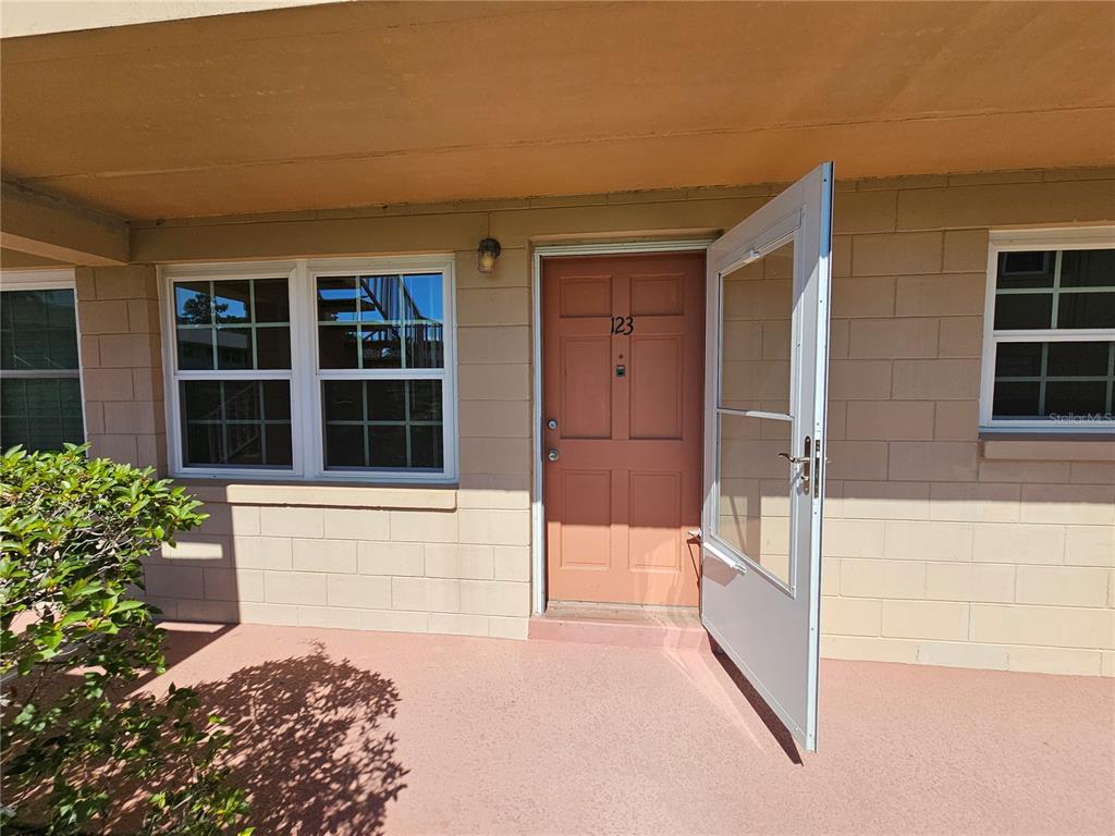 An exterior view of a tan building entrance with a peach door numbered 123 — 1100 E CAROLINE STREET UNIT 123, TAVARES, FL