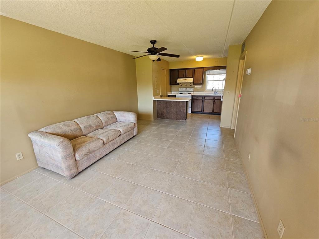 A living room with tile flooring and a sofa opens to a kitchen with cabinets — 1100 E CAROLINE STREET UNIT 123, TAVARES, FL