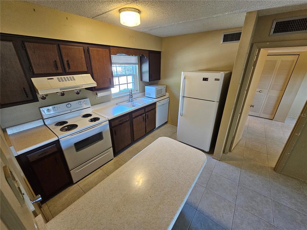 A kitchen features dark wood cabinets, white appliances, a peninsula, and light-colored tile flooring — 1100 E CAROLINE STREET UNIT 123, TAVARES, FL