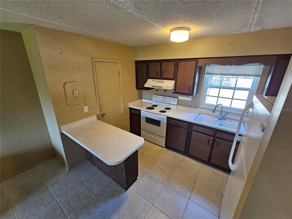 A kitchen with dark wood cabinets, white appliances, a peninsula, and light-colored tile flooring — 1100 E CAROLINE STREET UNIT 123, TAVARES, FL