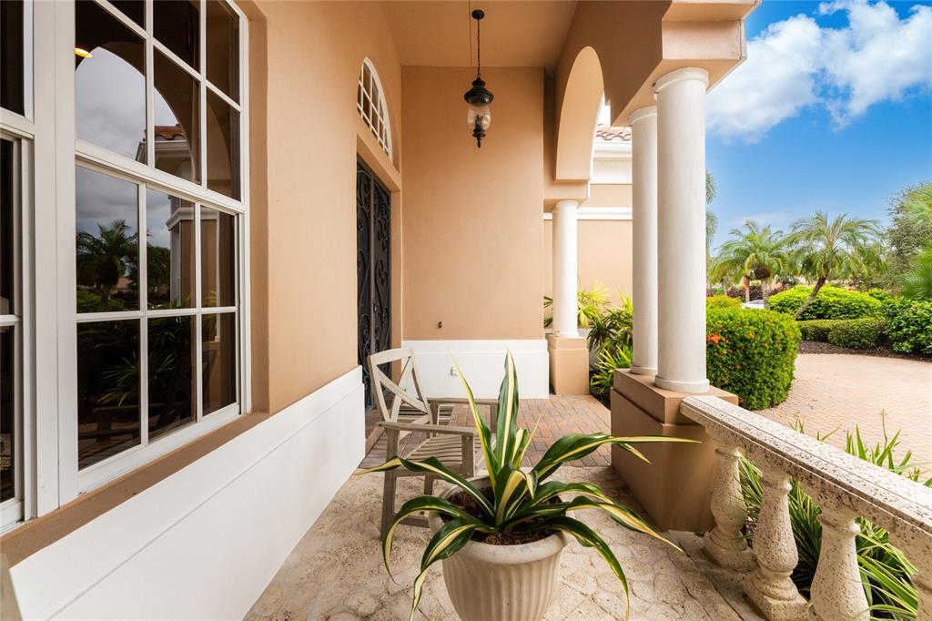 A covered porch with stone flooring, white columns, a potted plant, and a wooden chair — 10 BOCA ROYALE BLVD BOULEVARD, ENGLEWOOD, FL