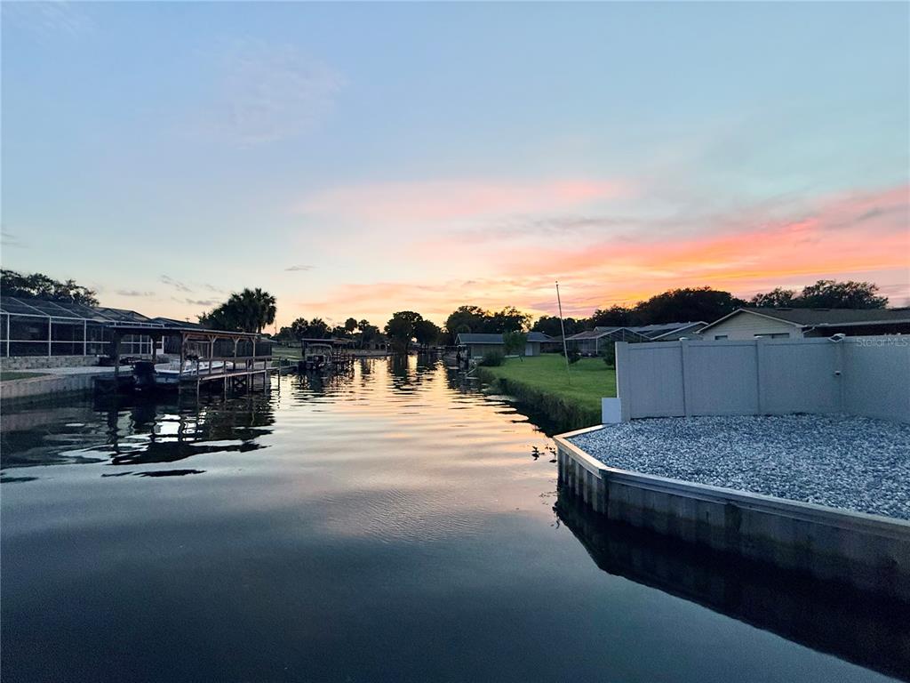 A canal view at sunset featuring a boat dock and a fenced backyard — 209 W DELAWARE STREET, TAVARES, FL