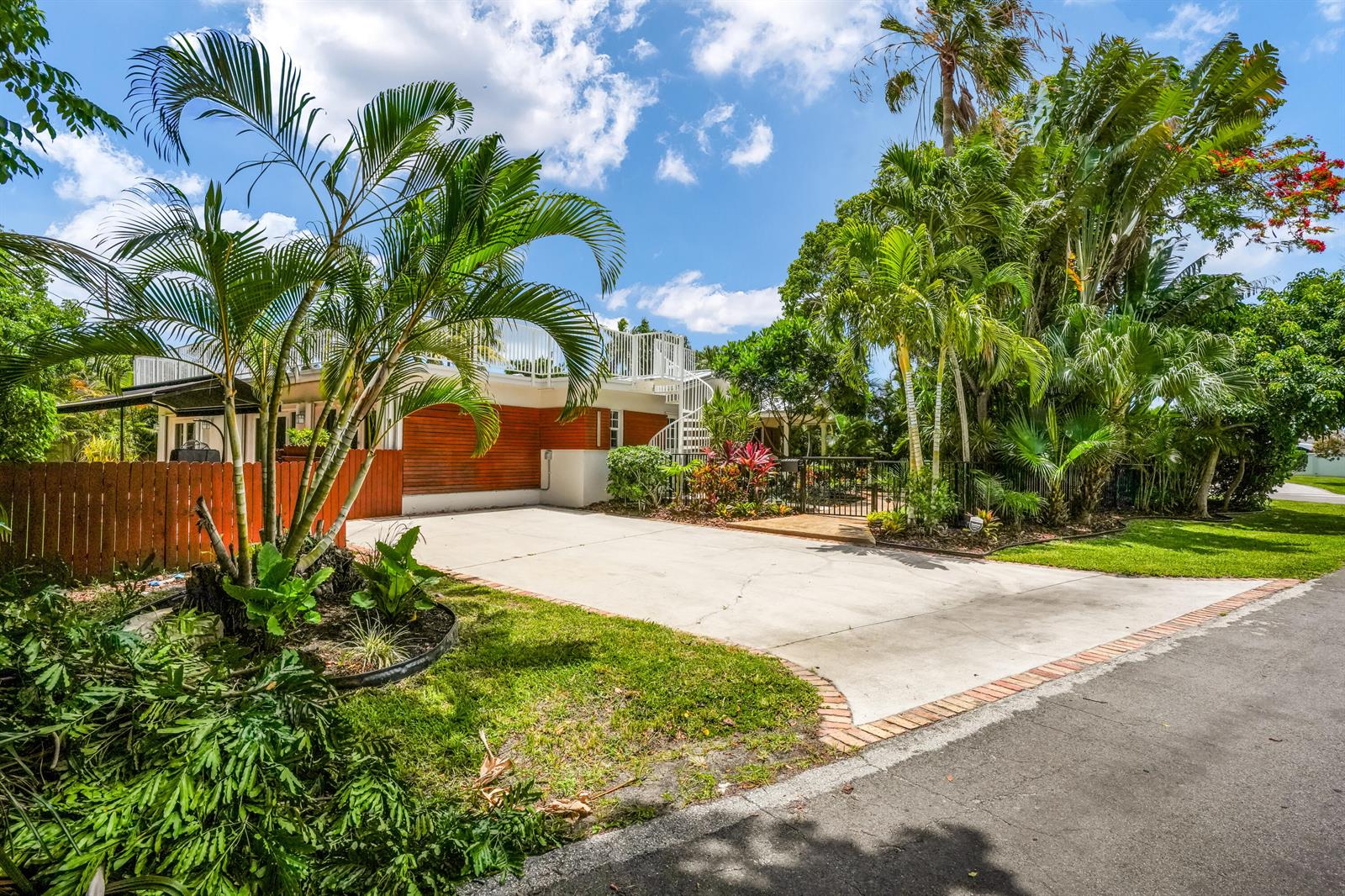 A concrete driveway leads to a house with wood siding, a spiral staircase, and landscaping — 2400 N Riverside Drive, Pompano Beach FL 33062, POMPANO BEACH, FL