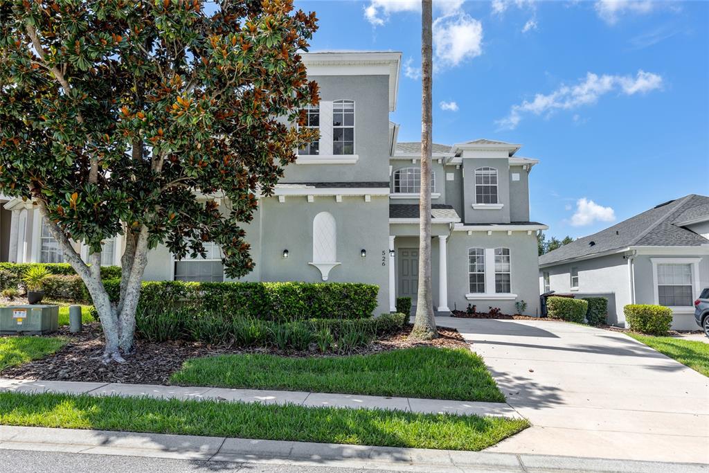 A two-story gray house with a concrete driveway, a large tree, and manicured landscaping — 526 PINELOCH DRIVE, HAINES CITY, FL