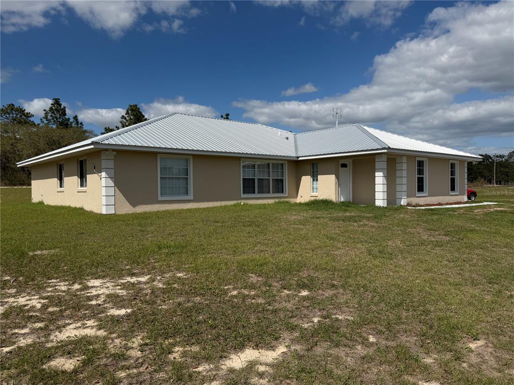 A single-story house with a light-colored stucco exterior and a metal roof — 7750 SE 150 AVENUE, MORRISTON, FL